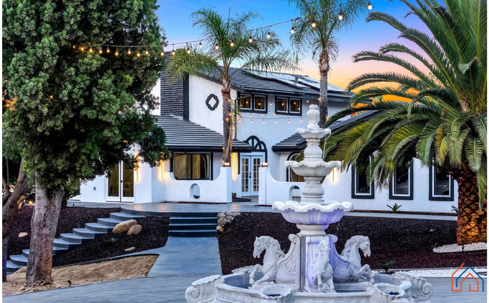 A completed two-storey home at twilight, with a tiled roof, arched entry, fountain and mature palms